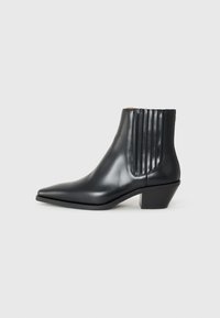Bottine en cuir noir avec un bout pointu, des panneaux latéraux élastiques avec des rainures verticales, et un petit talon bloc. Texture lisse et design épuré.