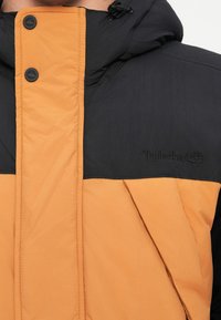 Crna i narančasta podstavljena jakna s kapuljačom, dugmadi na preklapanje i izvezenim Timberland logotipom na prsima.