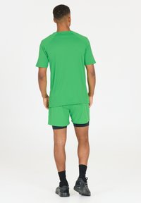 Groene sportshirt en short set, korte mouwen, gladde textuur, aangesloten ontwerp, gecombineerd met zwarte accenten op de shorts en sokken.
