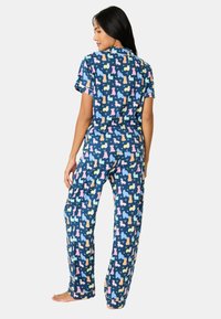 Marinblå pyjamasset med ett lekfullt hundtryck i olika färger. T-shirt med kort ärm och krage, löst sittande byxor med uppvikta nederkanter.