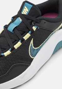 Sort mesh-sneaker med turkis og gul snøresystem, en syet swoosh-logo og en hvid sål med en struktureret blå detalje.