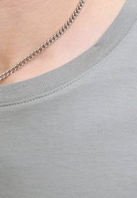 Grijze katoen t-shirt met een ronde hals, met een zachte textuur en subtiele stikdetails. Een zilveren kettinghalsketting is zichtbaar.