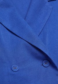 Blazer blu a doppio petto con bottoni rivestiti in stoffa e ampie rever, che mostra la texture dettagliata del tessuto tessuto.