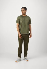 Olivengrønn T-skjorte med et subtilt mønster, kombinert med matchende bukser. Antrekket kompletteres med grå og oransje trening sko.