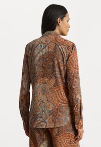 Brown paisley-patterned shirt with long sleeves, a collar, and button accents. Made of smooth fabric with intricate blue and orange designs.