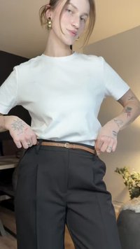 Wit katoenen t-shirt gecombineerd met zwarte broek met hoge taille. Een bruine leren riem met een ronde gesp maakt de outfit compleet.