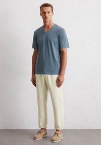 T-shirt bleu clair à col en v et manches courtes, assorti à un pantalon crème décontracté et à des chaussures beiges à lacets avec une surface texturée.