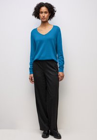 Turkoss v-ringad tröja och mörkgrå vida byxor. Tröjan har långa ärmar och en avslappnad passform; byxorna har en slät yta och en subtil struktur.