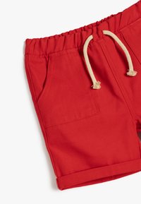 Pantaloni corti rossi in tessuto texturizzato, con vita elastica e cordino, due tasche laterali e orli arrotolati.