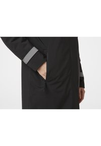 Černá bunda s kapsou na zip a reflexními akcenty na rukávech. Vyrobena z hladkého, voděodolného materiálu.