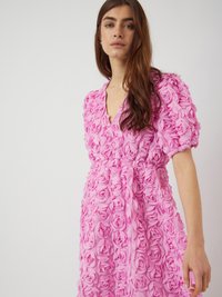 Rosa klänning täckt av texturerade, lager-på-lager rosapplikationer. Djup V-ringning, puffärmar och insydd midja framhäver den blommiga designen.