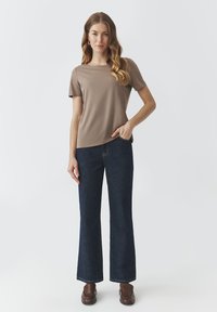 Top beige a maniche corte abbinato a jeans a palazzo blu scuro. Il top ha un collo rotondo e i jeans presentano una classica texture in denim.