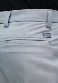 Κοντινό πλάνο ανοιχτόγριλων παντελονιών με πίσω τσέπη welt και μικρό ορθογώνιο λογότυπο BOSS κοντά στη μέση.