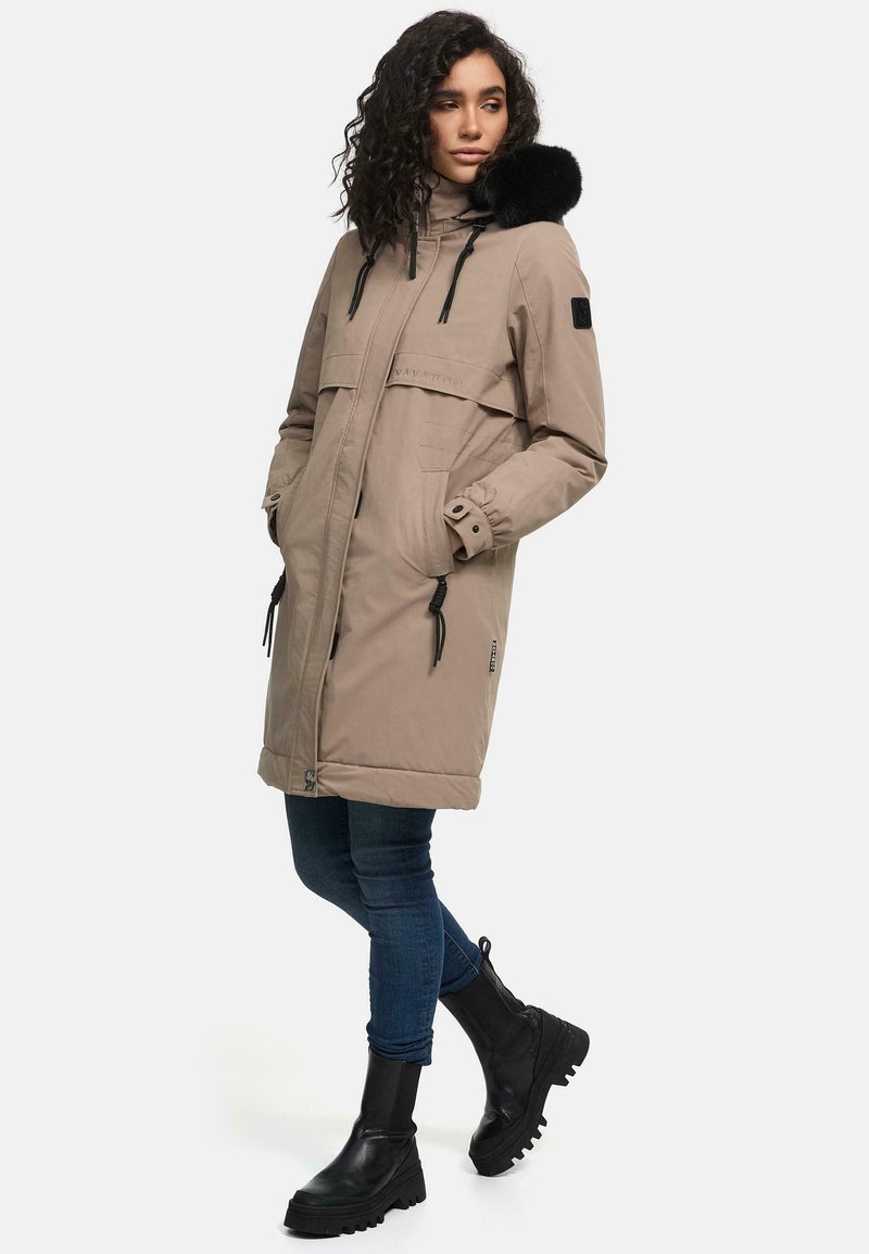 Kaki parka jakna s kapuljačom obloženom crnim krznom, prednjim džepovima, podesivim vezicama i opuštenim krojem. Nosi se preko tamnih traperica i crnih čizama.