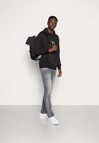 Sort hættetrøje med grafisk detalje, grå slim-fit jeans og hvide sneakers. Bærer en sort rygsæk med et struktureret design.