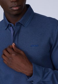 Polo shirt bleu marine en tissu texturé, avec des rayures contrastées au col et un petit logo brodé près de la poitrine.