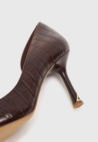 Chaussure à talons hauts en cuir marron avec texture crocodile, bout pointu allongé et talon aiguille brillant avec accent doré.