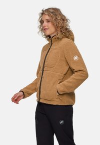 Brun fleecetröja med huva, med dragkedja fram, stor ficka och logopatch på ärmen. Svarta detaljer vid ärmsluten.