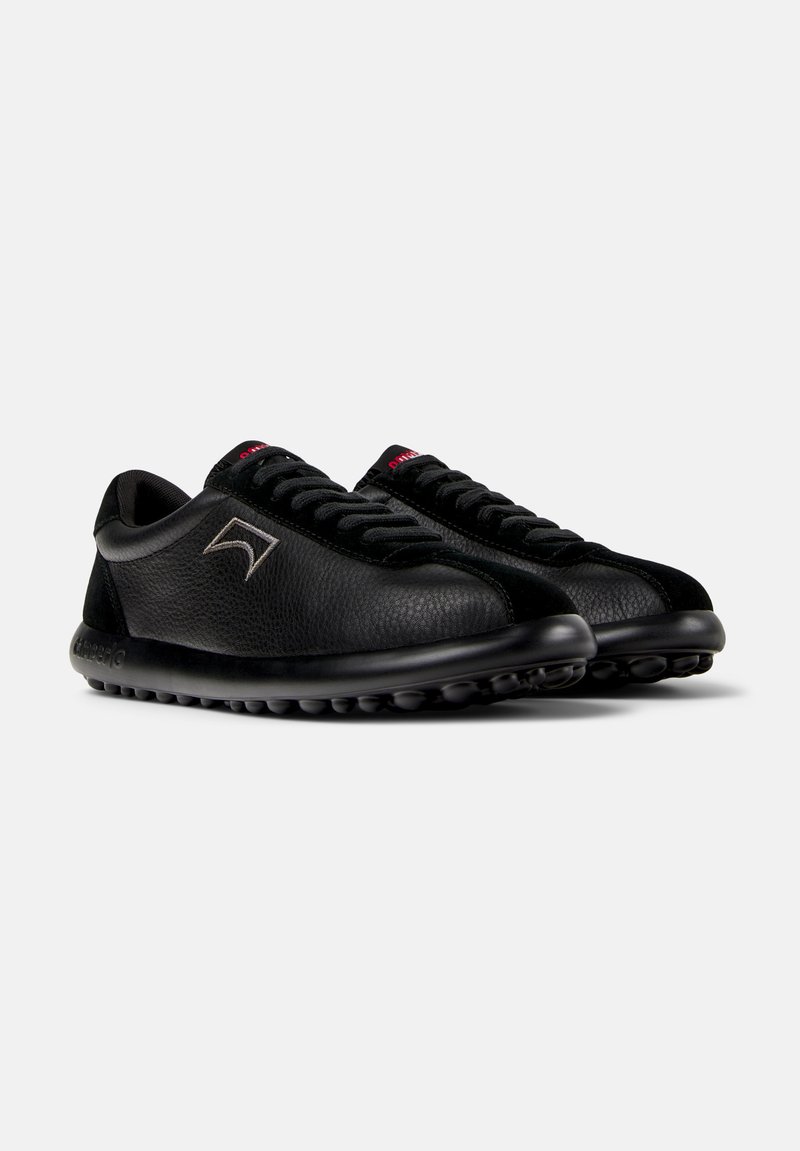 Zwarte leren sneakers met een gestructureerd oppervlak, voorzien van een ronde neus, zwarte veters en een flexibele zool met kleine knoppen voor grip.