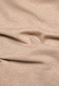 Beiges Strickgewebe mit weicher Textur, versehen mit einem gerippten Saum. Das Gewebe zeigt sanfte Falten, die auf einen guten Fall und leichte Eigenschaften hinweisen.