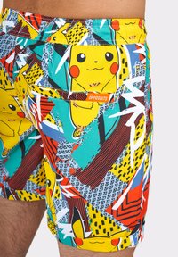 Farebné plavky s dizajnom Pikachu, vyrobené z jemnej tkaniny, s živou abstraktnou potlačou v žltej, zelenej, červenej a modrej farbe.