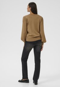 Pull marron avec des manches bouffantes côtelées, associé à un jean noir et des mocassins noirs. Design simple, texture lisse et coupe décontractée.