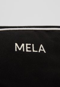 Black fabric bag with a textured surface, featuring the embroidered white text "MELA" and a contrasting white zipper trim.