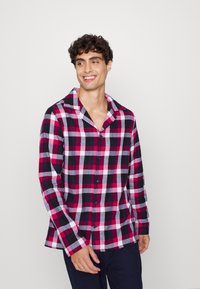Karierte Flanellbluse in Rot, Schwarz und Weiß mit einem Schalkragen, langen Ärmeln und Knopfverschluss. Weiche Textur, lockere Passform und sichtbare Nähte.