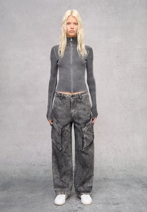 Fitted grijs gestreepte ribgebreide ritssluiting top en losse grijze cargobroek met zakken, gecombineerd met witte sneakers. Achtergrond is minimalistisch grijs.