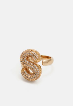Goldfarbener Ring mit einer strukturierten, geschwungenen 'S'-Form, die mit kleinen klaren Edelsteinen verziert ist. Glatte Band mit polierter Oberfläche.