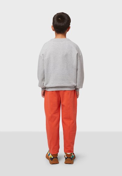 Sudadera gris con mangas anchas, combinada con pantalones de chándal naranjas. El conjunto se completa con zapatillas multicolores y un diseño texturizado.