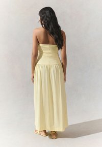 Abito lungo giallo con corpetto aderente e gonna svasata, realizzato in tessuto leggero. La parte posteriore presenta una cerniera e una texture liscia.