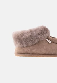 Chausson beige avec un col en fourrure grise douce et duveteuse, en matière suédée, de forme arrondie et avec une semelle texturée et durable.