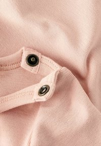 Zbliżenie na miękką, jasnoróżową tkaninę, z dwoma czarnymi zatrzaskami i szczegółowym przeszyciem wzdłuż krawędzi.