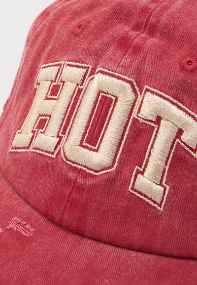 Casquette de baseball en tissu rouge avec broderie "HOT" en crème. Présente une finition légèrement usée et une visière incurvée.