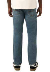 Niebieskie dżinsy z prostymi nogawkami, z dwoma tylnymi kieszeniami i subtelnym efektiem przetarcia. Nosi się je z czarno-białymi trampkami.