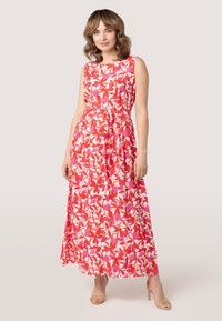 Maxi-jurk in een rood-witte bloemenpatroon, met een aansluitende taille en zonder mouwen ontwerp. Lichte stof die tot op de enkels valt.
