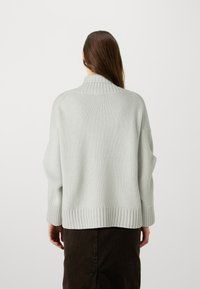 Pull en maille gris clair avec un col et un ourlet côtelés, doté de manches tombantes et de longues manches, porté sur une jupe sombre à texture.