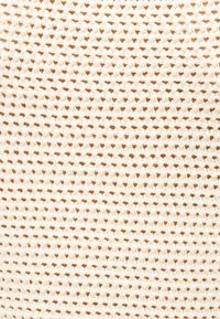 Πλεκτό ύφασμα σε κρεμ χρώμα με μικρό, επαναλαμβανόμενο μοτίβο που μοιάζει με βάφλα, δημιουργώντας υφασμάτινα τετράγωνα.