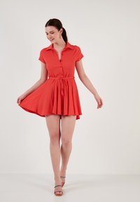 Red button-down dress with short sleeves, a waist tie, and flared skirt. Textured fabric and subtle pleating detail at the hem.