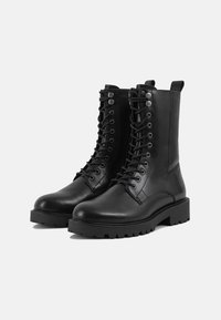 Schwarze Leder-Kampfstiefel mit hohem Knöchel, runder Spitze, Schnürung vorne, verstärkten Ösen und strukturiertem Gummisohle. Mit einer Schlaufe an der Rückseite.