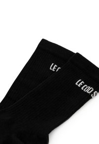 Calcetines de algodón negros con textura acanalada y letras blancas que dicen "LE COOD". El diseño es simple y clásico.