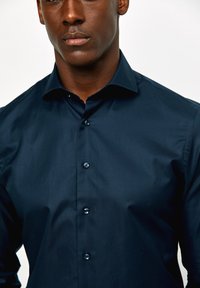 Donkerblauwe blouse met knopen in een gladde stof, voorzien van een puntige kraag en zes donkere knopen aan de voorkant. Slim fit.