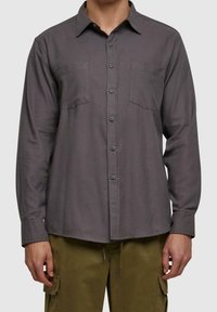 Szara koszula z długim rękawem, zapinana na guziki, z dwoma kieszeniami na piersi i ostrym kołnierzykiem. Miękki materiał o gładkiej fakturze.