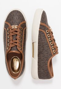 Braune Sneakers mit strukturierter Oberfläche, kontrastierenden braunen Akzenten, Schnürdesign und goldfarbenem Markenlogo. Verfügen über eine weiße Gummisohle.