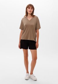 Hladký krémový top s výstřihem do V a krátkými rukávy, spárovaný s černými kraťasy a bílými teniskami. Příjemný materiál s volným střihem.