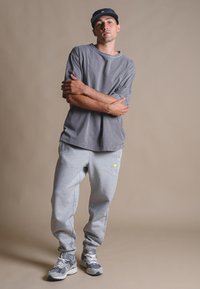 T-shirt in cotone grigio oversize, pantaloni jogger in pile grigi con polsini elasticizzati e sneakers grigie con dettagli bianchi. Design casual e fits rilassato.