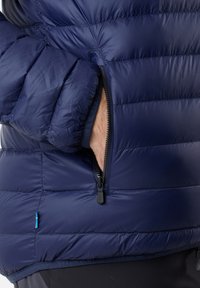 Marineblauer isolierter Mantel mit einem gesteppten Design, ausgestattet mit einer mit Reißverschluss versehenen Tasche und einer weichen Textur. Mit einem kleinen Akzentanhänger.