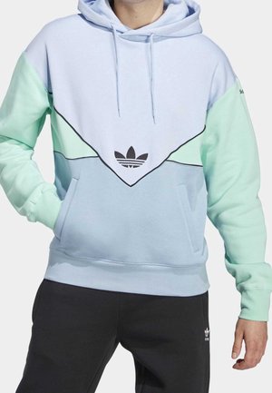 Mann trägt einen Farbblock-Kapuzenpullover in Pastellblau, Mint und Weiß mit Adidas-Logo auf der Brust, kombiniert mit schwarzen Adidas-Hosen.