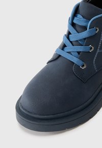 Stivaletto blu navy realizzato in materiale sintetico liscio, con punta rotonda, lacci blu e cuciture a contrasto sui lati.